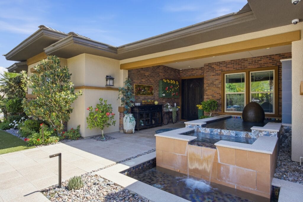 Custom backyard with outdoor kitchen, spa, water features, and desert landscaping adjacent to modern home.