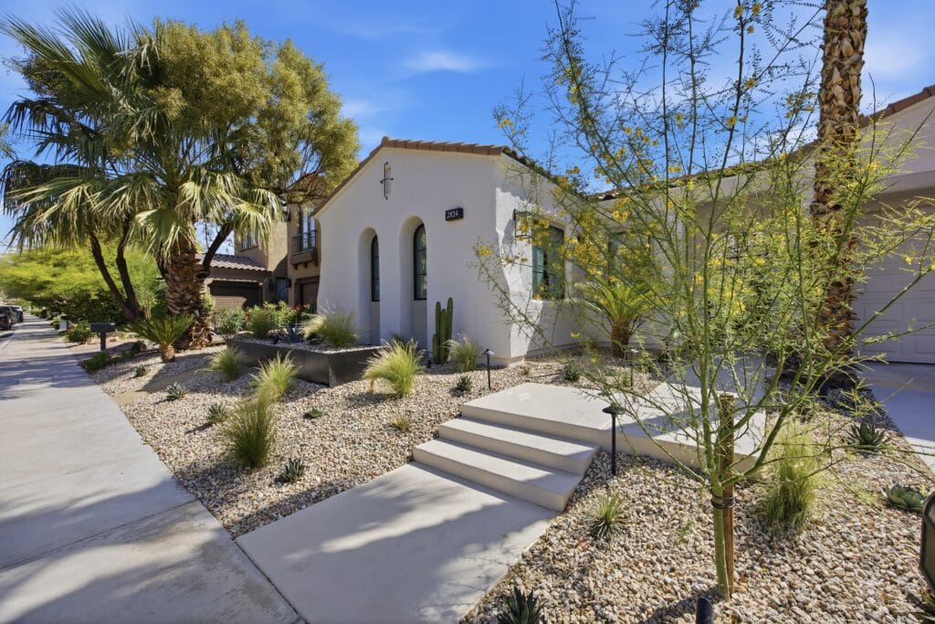 Modern white home with desert landscaping, palm trees, and gravel hardscape in bright sunlight.