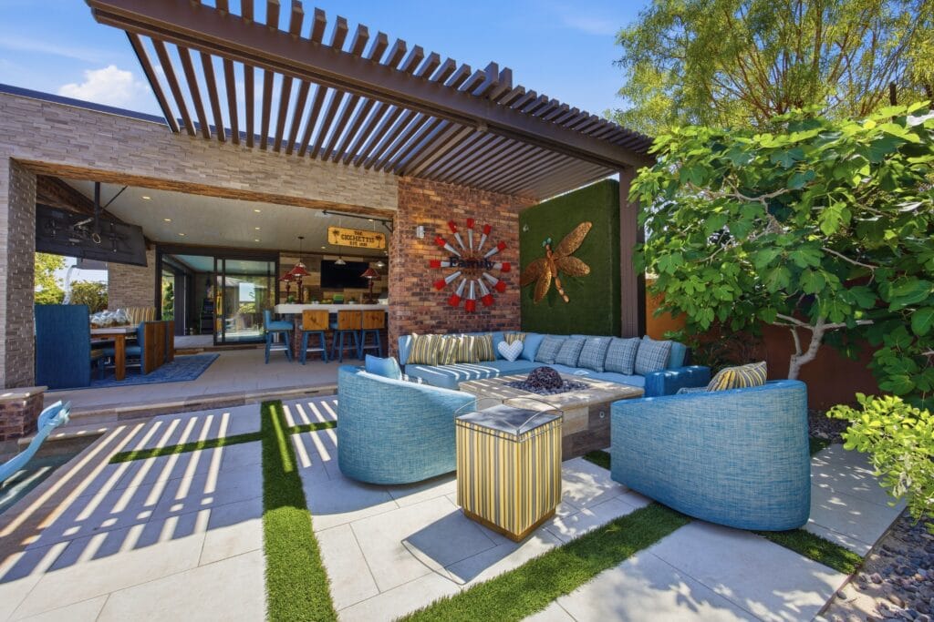 Modern outdoor living space with curved blue seating, pergola shade structure, brick accent wall, and lush landscaping.