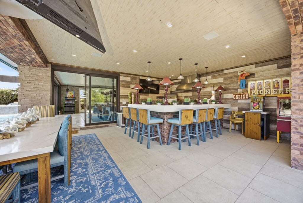 Spacious covered outdoor entertaining area with bar seating, kitchen appliances, and decorative gaming signs.