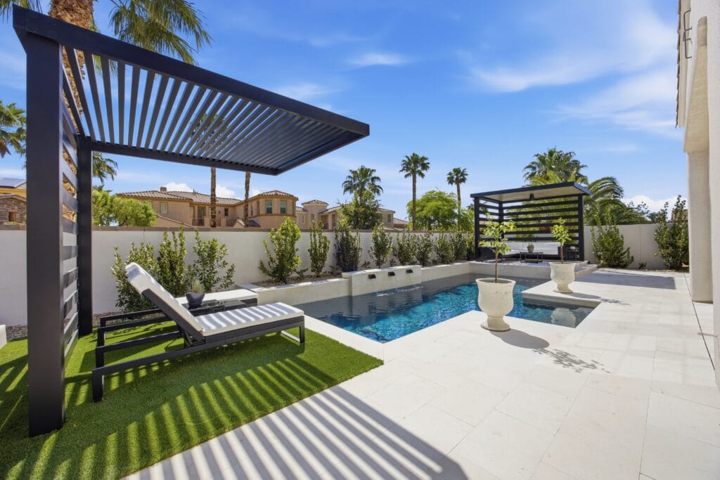 Modern backyard with custom swimming pool, spa, lounge chairs, pergolas, and manicured landscaping.