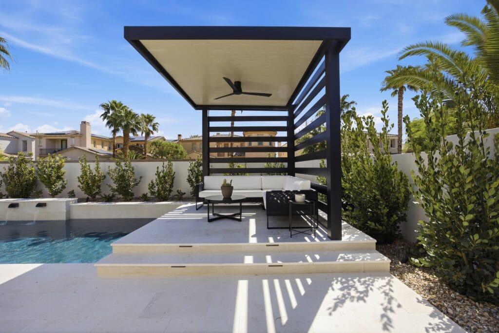Modern backyard patio with pool, black pergola with ceiling fan, lounge seating, and desert landscaping.