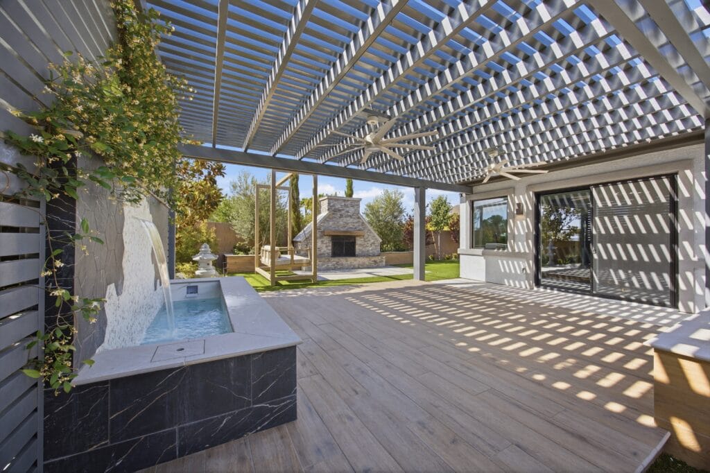 Modern pergola-covered patio with spa, lounge seating, and manicured desert landscape view.