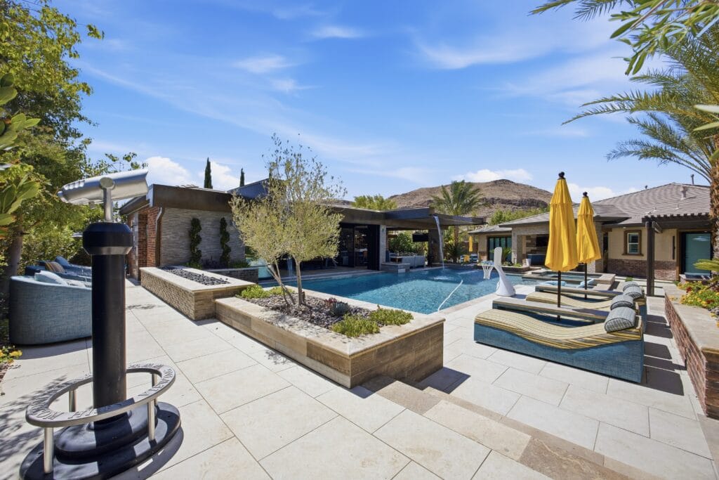 Luxurious resort-style backyard with sparkling pool, spa, lounge areas, yellow umbrellas, and modern hardscaping surrounded by desert landscaping.