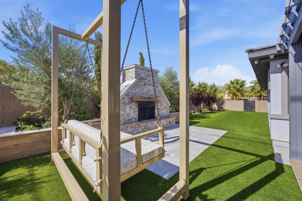 Elegant backyard with a wooden pergola swing, stone fireplace, manicured lawn, and modern landscaping design.