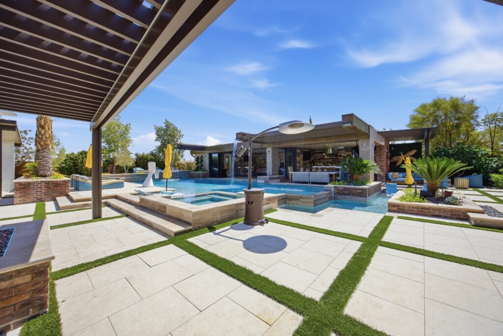 Luxurious backyard oasis featuring a custom pool, spa, waterfall, pergola, outdoor kitchen, and manicured landscaping.