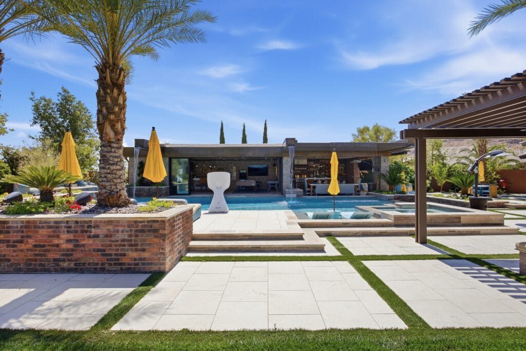 Luxury backyard featuring a resort-style pool with spa, modern lounge areas, yellow umbrellas, and manicured landscaping.