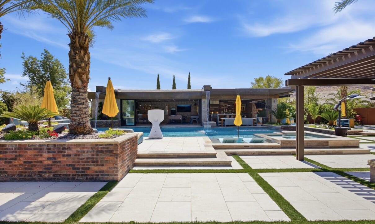 Luxury backyard featuring a resort-style pool with spa, modern lounge areas, yellow umbrellas, and manicured landscaping.