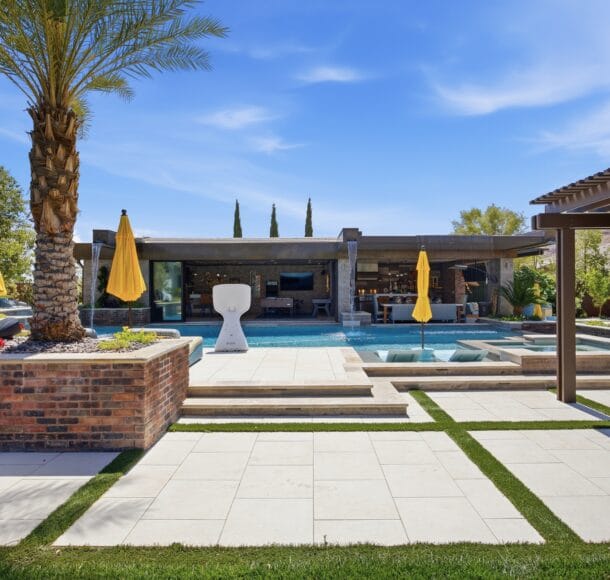 Luxury backyard featuring a resort-style pool with spa, modern lounge areas, yellow umbrellas, and manicured landscaping.