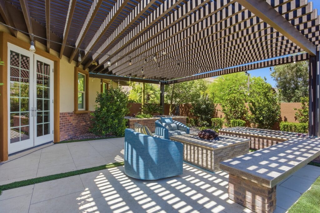 Covered patio with pergola, blue chair, built-in bench seating, and striped shade patterns over light tile flooring.