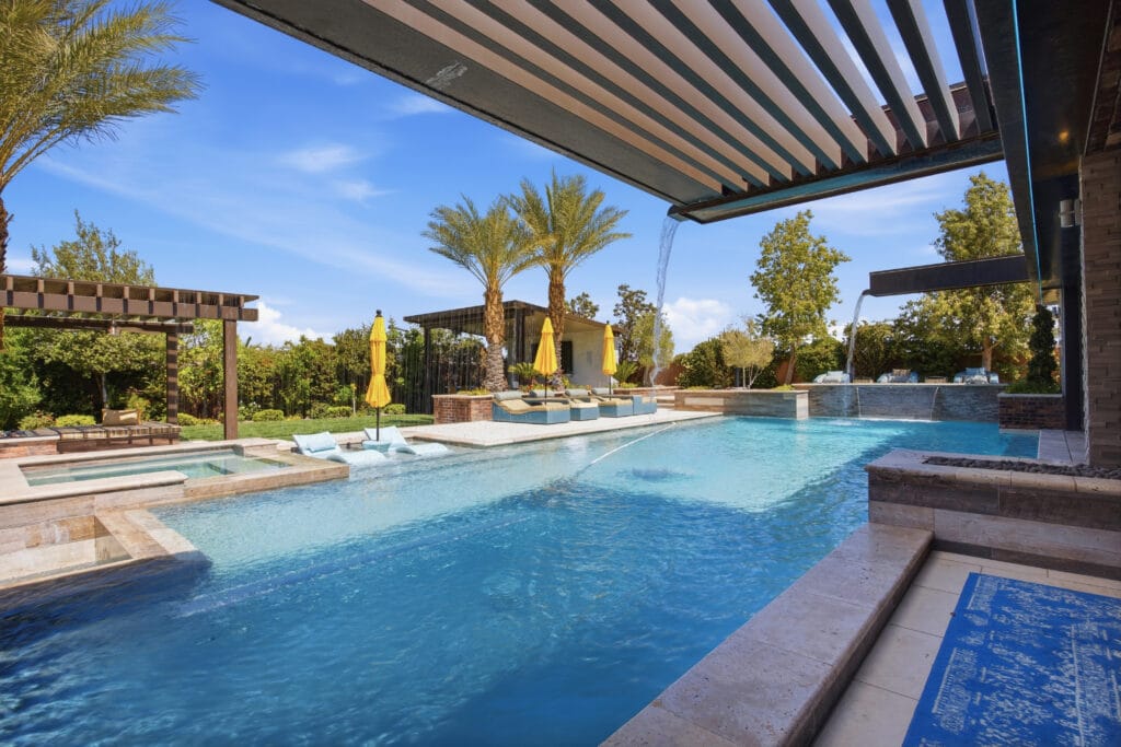 Luxurious backyard pool and spa surrounded by palm trees, lounge seating, and modern pergola shade structures.