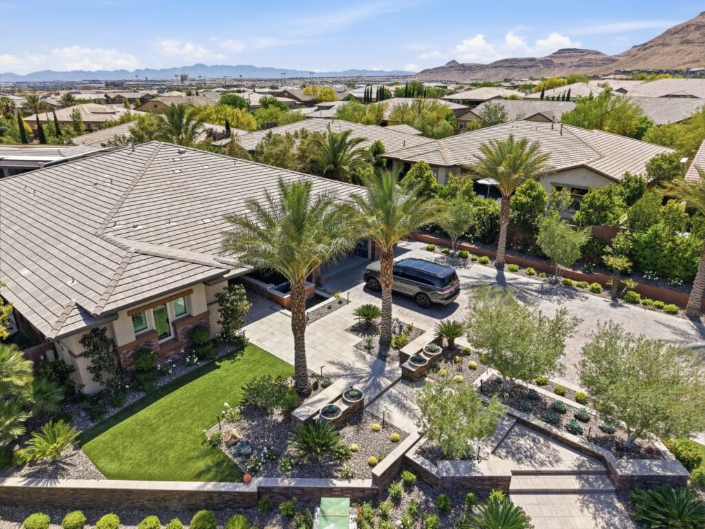 Aerial view of a modern desert home with manicured landscaping, palm trees, and a spacious backyard featuring hardscape design.