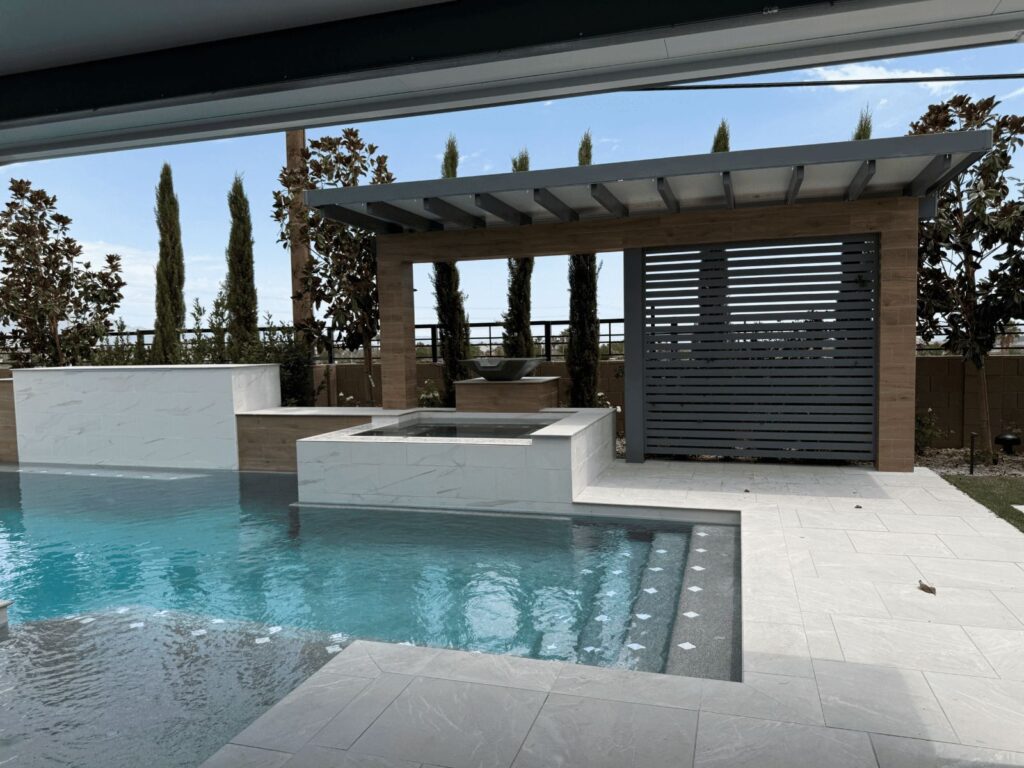 Modern luxury pool with spa, pergola, lounging area, and cypress trees in contemporary desert landscape design.